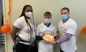 Two Eden staff members, a male and female, present a cake to a participant. 